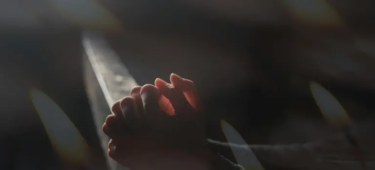 Two hands clasped together in a vigil with glowing candles in the background
