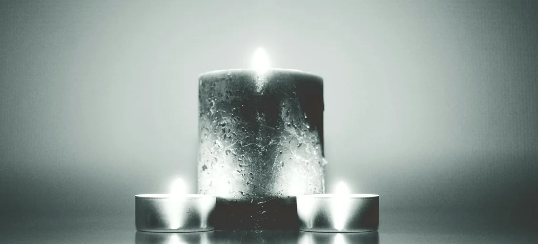 A central tall candle flanked by two smaller candles, all lit, against a soft, muted background.