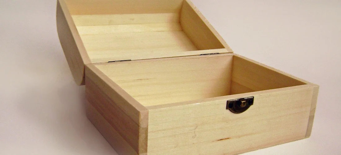 Light-colored wooden casket-like box opened to reveal two interior compartments against a pale background.