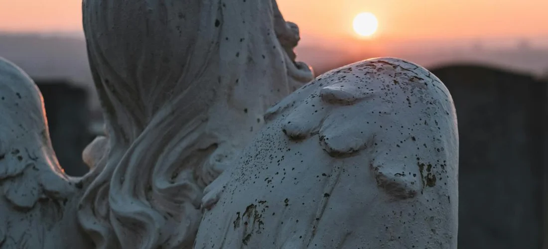 Close-up of a weathered angel statue in a cemetery at sunset.