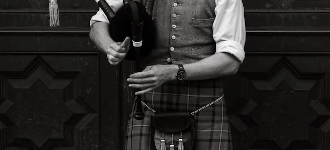 A person in traditional Scottish attire (kilts and vest) holding bagpipes