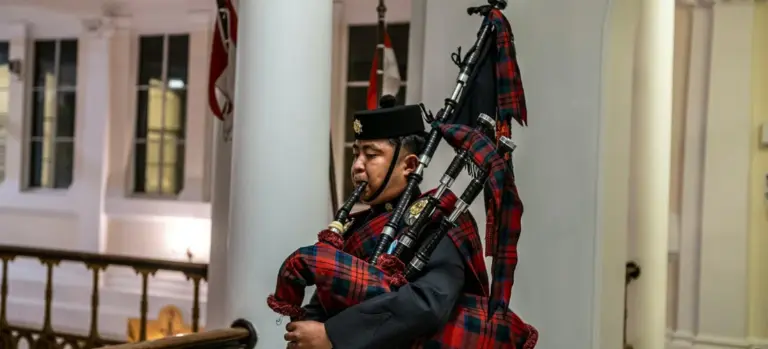 A Scottish bagpiper in formal attire playing bagpipes at a funeral ceremony