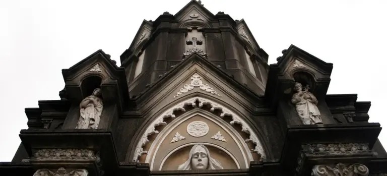 Gothic church facade with statues and arched details against a cloudy sky.