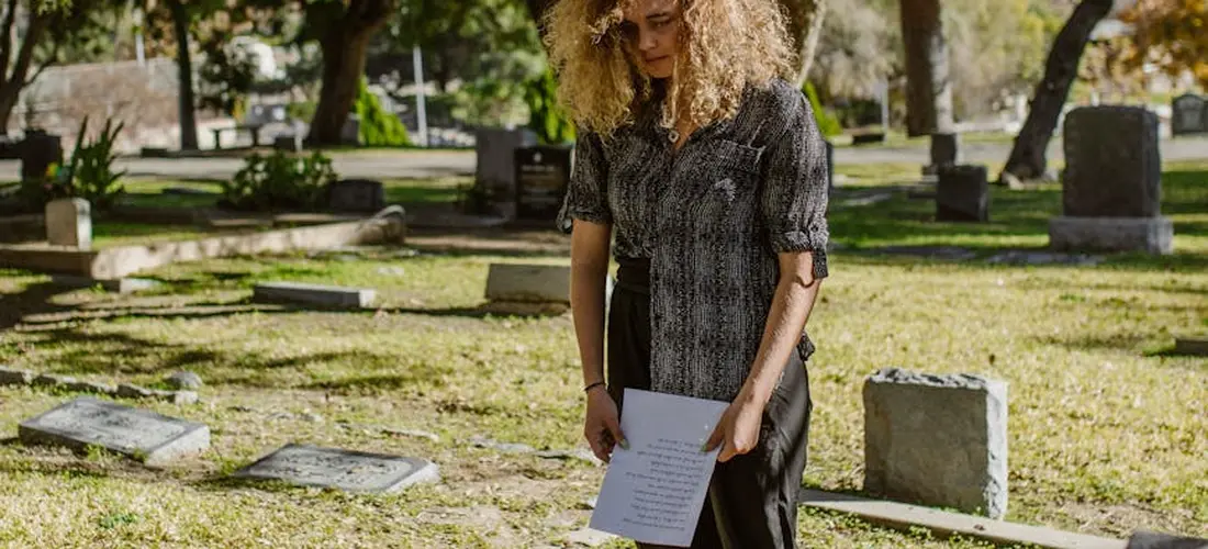 A person stands in a cemetery holding a document, illustrating evaluating funeral expenses paid from an estate.