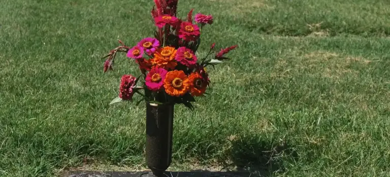 Colorful bouquet of flowers in a black vase placed on a grassy memorial area.