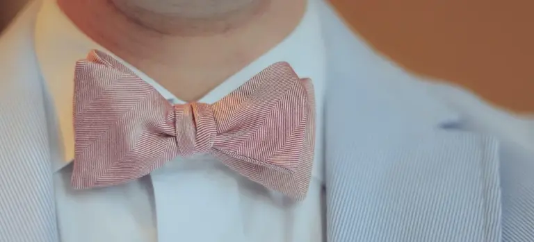 Close-up of a man’s chest wearing a light blue blazer and a pink bow tie, representing formal funeral attire.
