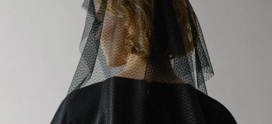 A person is shown from behind wearing a black veil and dark clothing, suggesting respectful funeral attire.