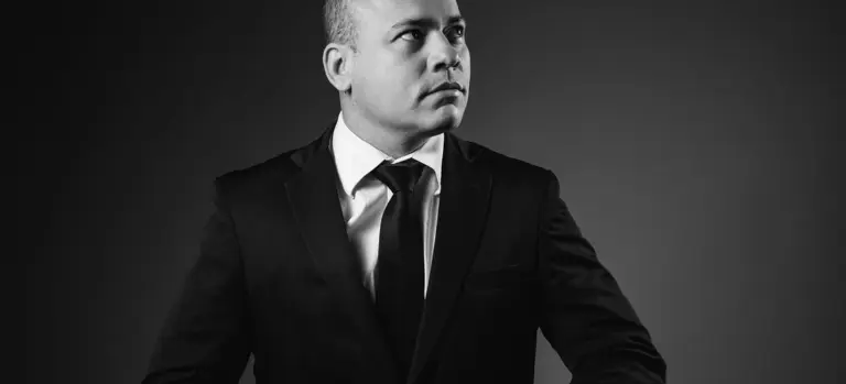Black-and-white photo of a man in a dark suit and tie looking to the side.