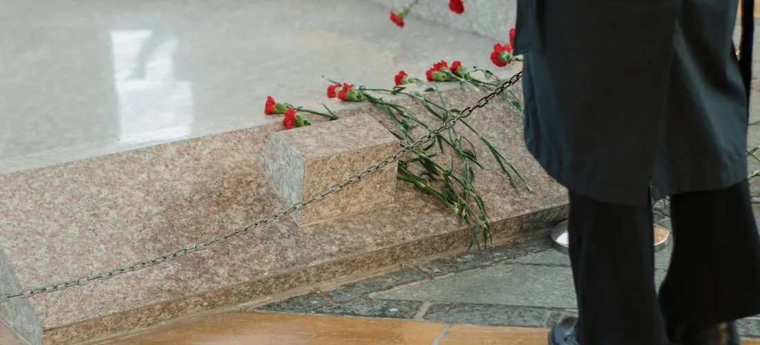 A figure in formal attire near red roses placed on a marble step at a funeral.