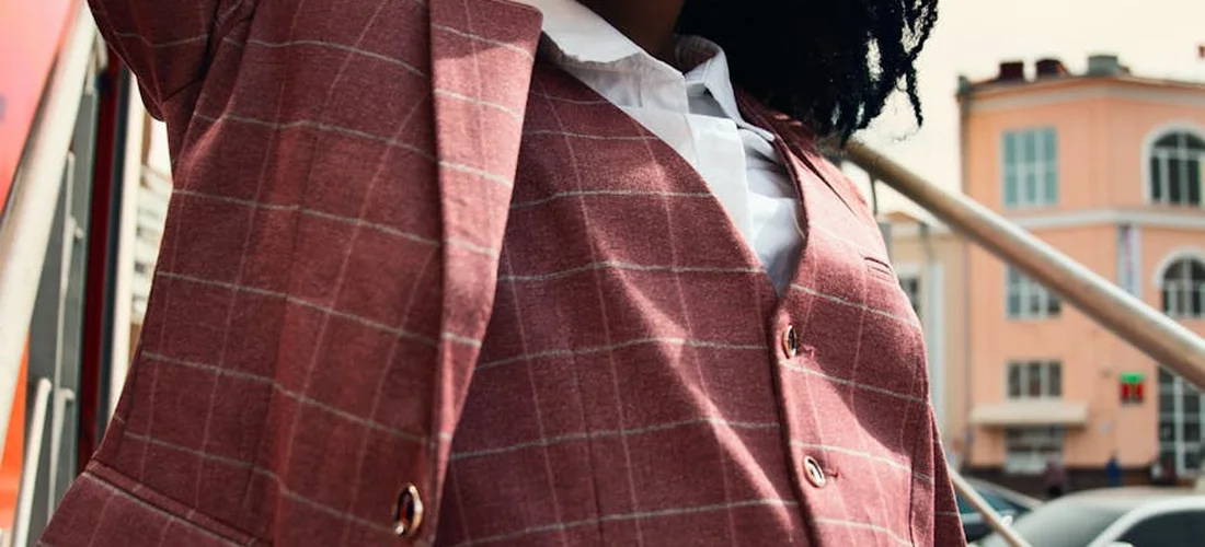 Close-up of a person wearing a pink plaid blazer and white shirt, standing outdoors near a staircase.