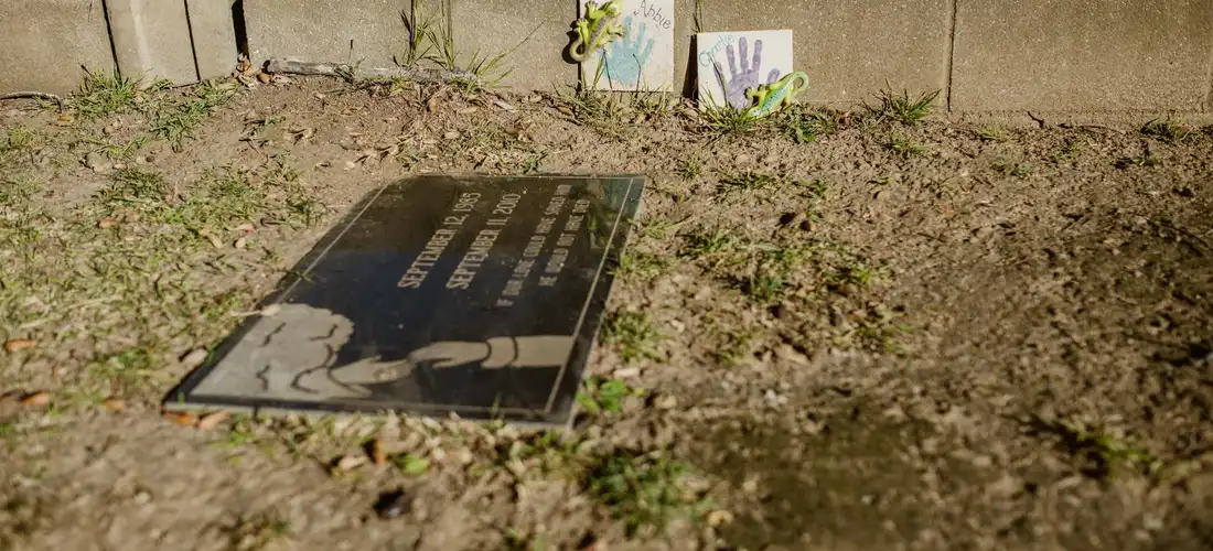 A flat memorial plaque on dirt in a graveyard, with small handmade cards propped up in the background.