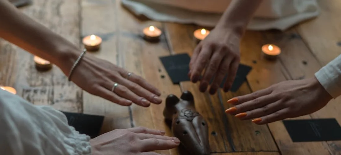 Several hands reach toward a carved keepsake on a wooden table, surrounded by candles and small cards, suggesting a memorial planning moment.