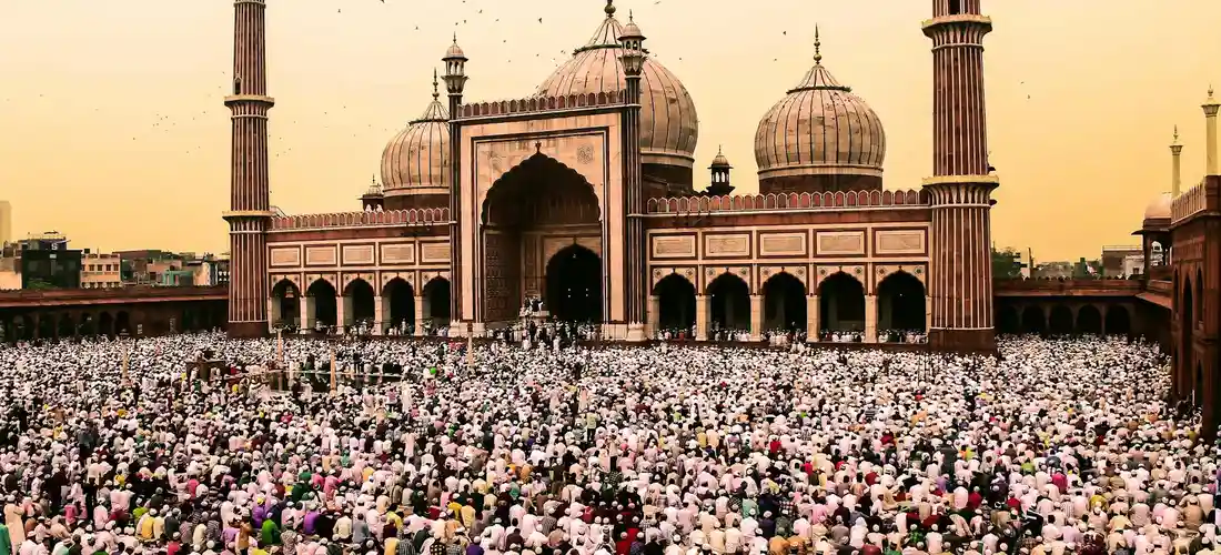 A large crowd of worshippers gathered in a grand mosque, forming rows for a congregational prayer