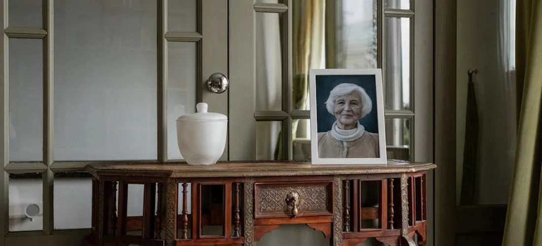 Framed portrait of an elderly woman on a wooden table with a small white vase, set in a softly lit room