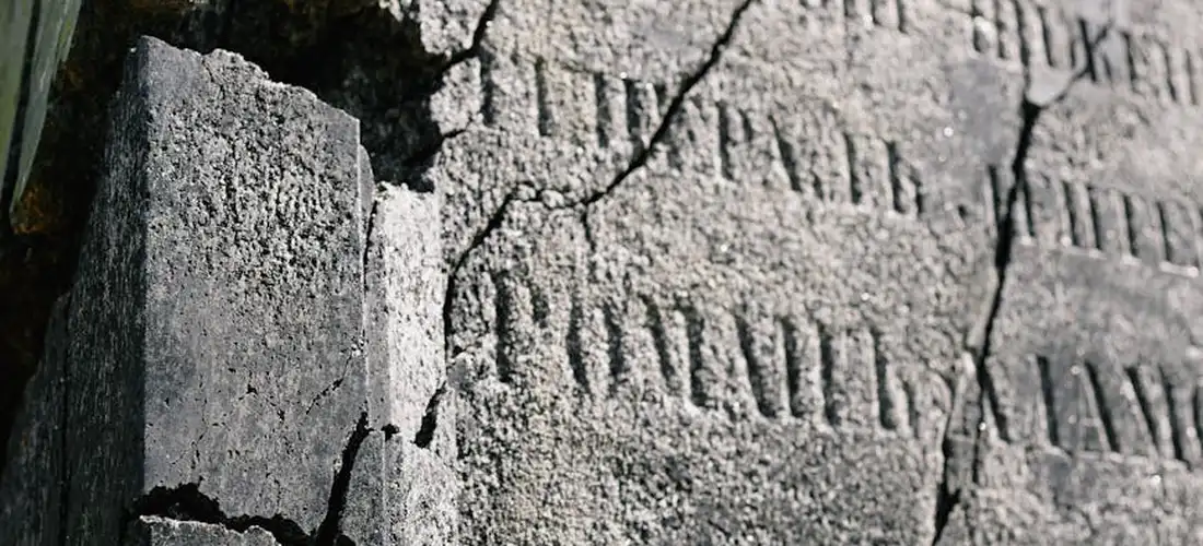 Weathered cemetery stone with faded inscriptions and cracks, suggesting quiet contemplation about selling unused grave sites.