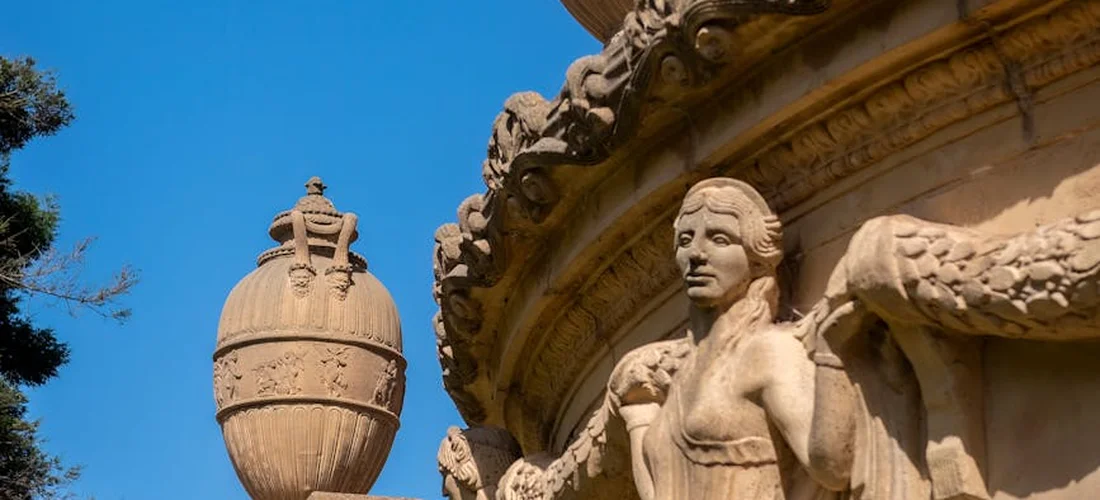 Stone fountain with a decorative urn and a carved statue against a blue sky